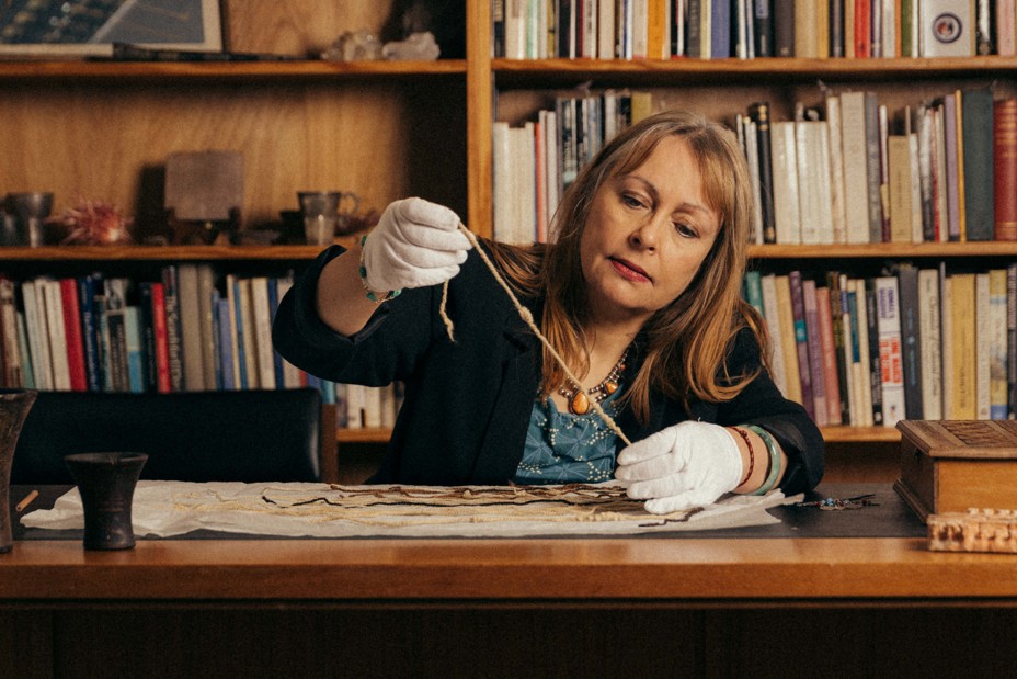 Sabine Hyland examines the chord of a khipus while wearing white gloves and sitting at a desk.