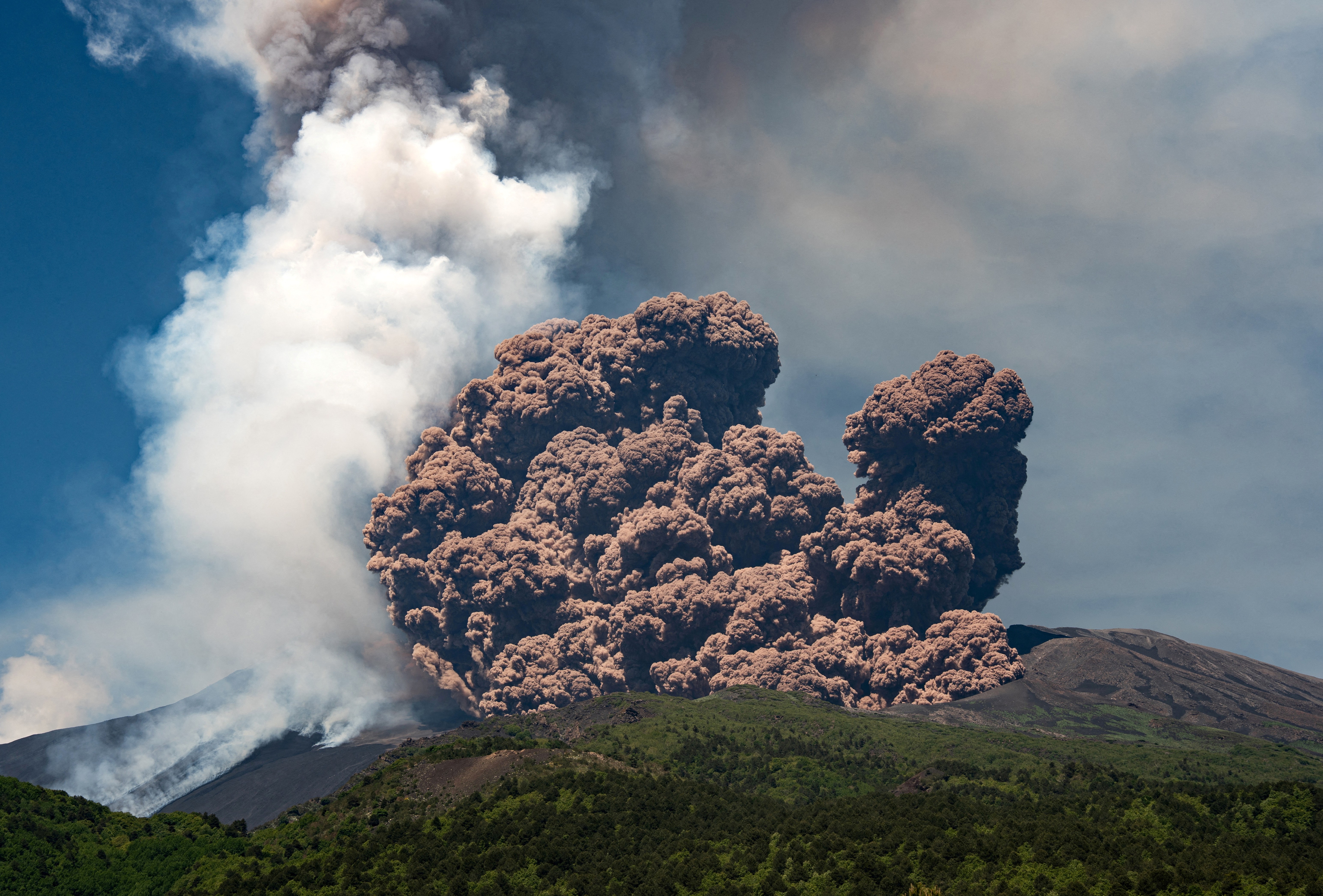 A large plume of brownish-colored ash rises from the top of a volcano.