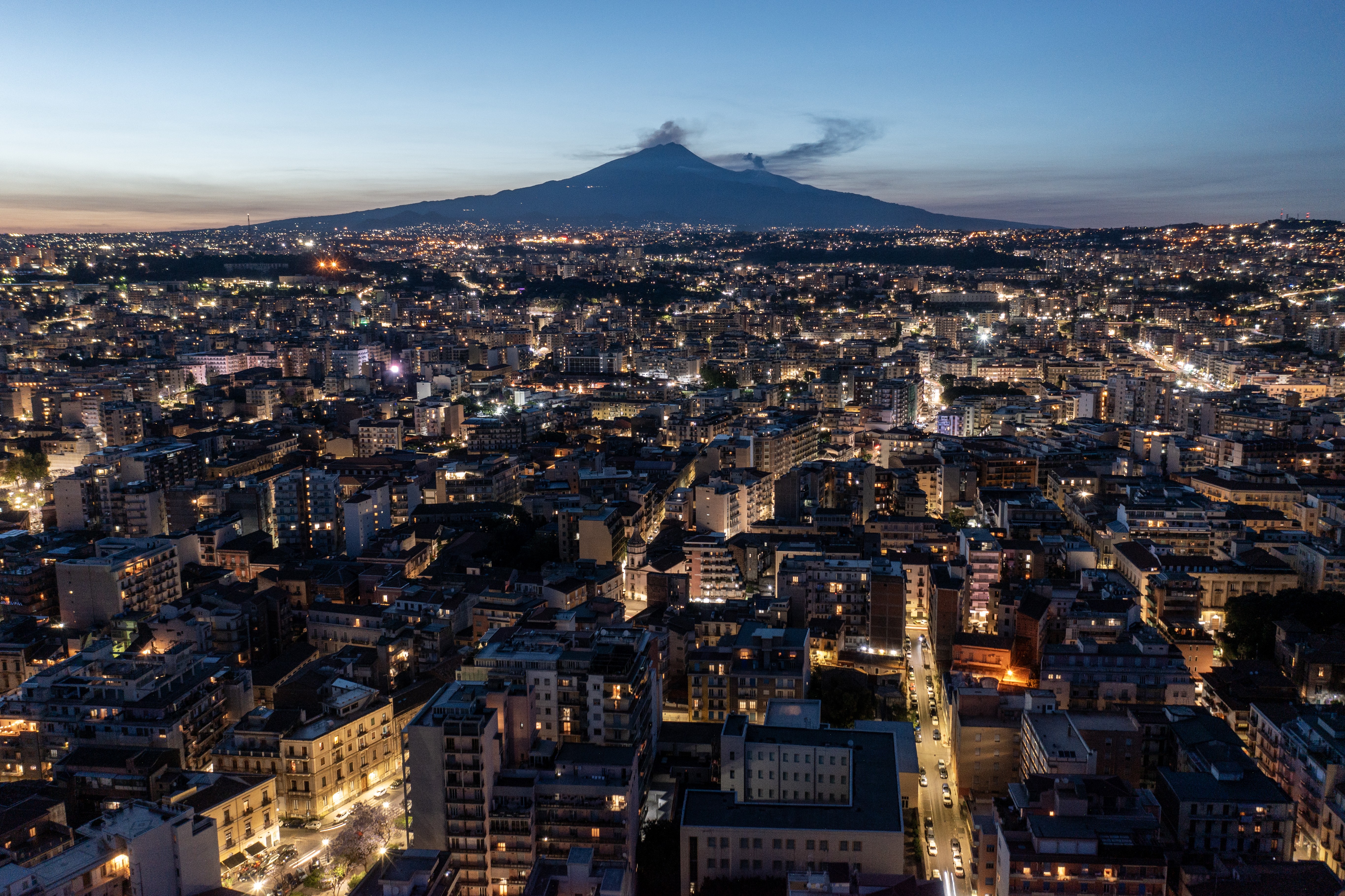 A calmer Mount Etna, seen at sunset from across a city.